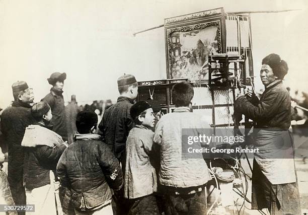 Peiping, China: View of a Mongolian showman turning the crank of his portable movie house, and charging the youngsters of the town the equivalent of...