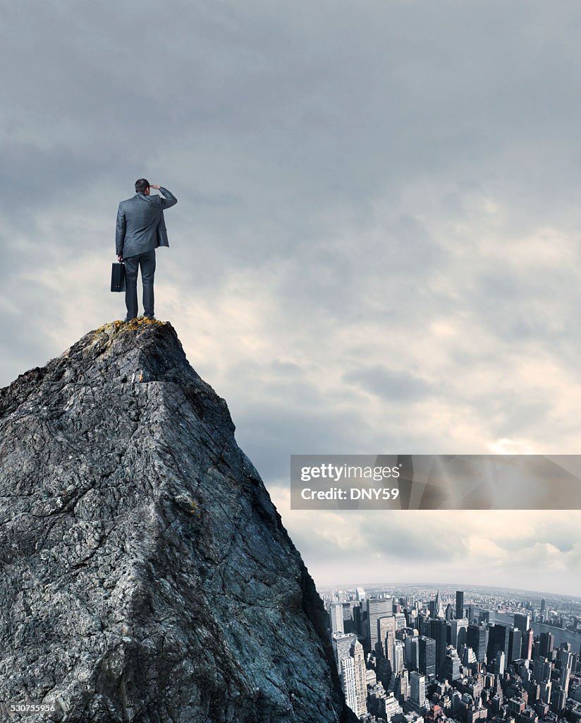 Homme d'affaires regardant la grande ville, tout en restant au sommet de la montagne
