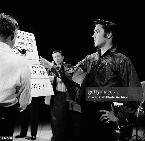 American singer and musician Elvis Presley , guitar around his neck, looks over a cue card while on 'The Ed Sullivan Show,' Los Angeles, California,...