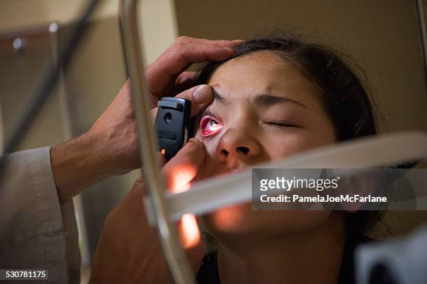 doctor examines patient's eye in dark room with handheld lens - vouyer stock pictures, royalty-free photos & images