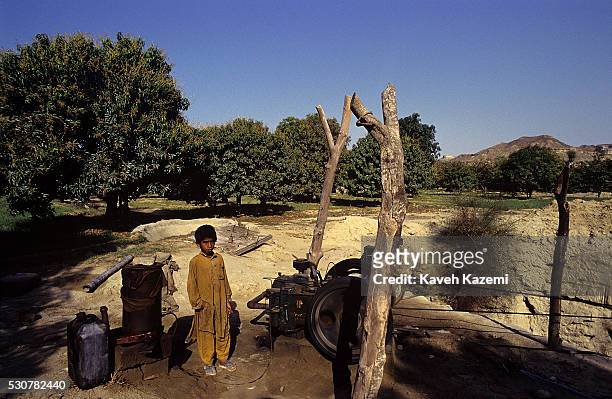 Typical Baluch boy in traditional costume stands next to an old fashioned water pump for irrigation in the port city of Chabahar in southeast Iran,...