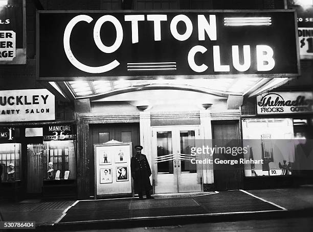 Exterior view of the Cotton Club nightclub , where a uniformed doorman stands under the venue's illuminated marquee, New York, New York, late 1930s....