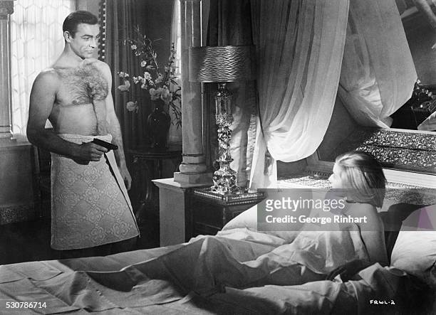 Towel-clad James Bond gets the drop on Tatiana Romanov lying in bed, in From Russia with Love, second in the popular series of James Bond spy...