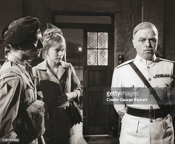 John Leyton , Mia Farrow , and Richard Attenborough starring in Guns at Batasi. This 1964 film was directed by John Guillermin.