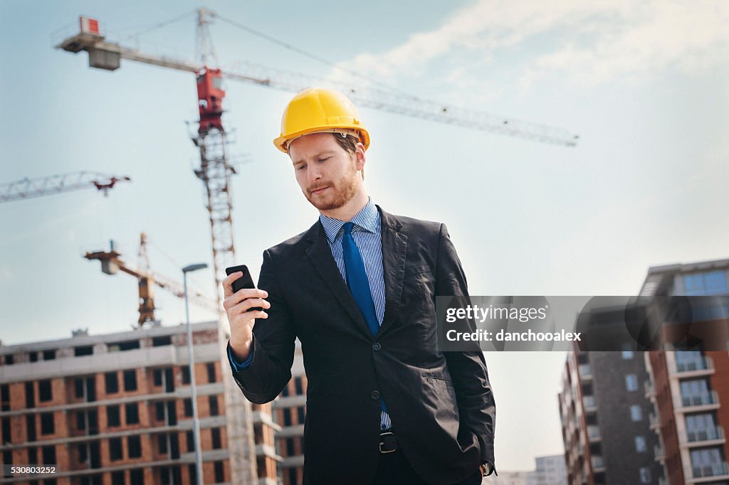 Engenheiro no local de construção usando smartphone