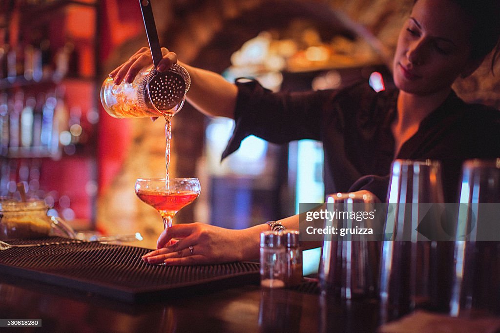 Young female bartender pouring cocktails in a cocktail bar
