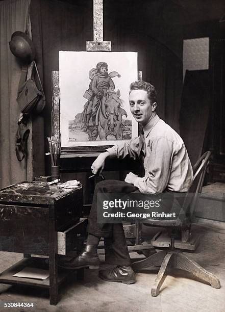 Photo shows painter Norman Rockwell seated in front of one of his paintings.