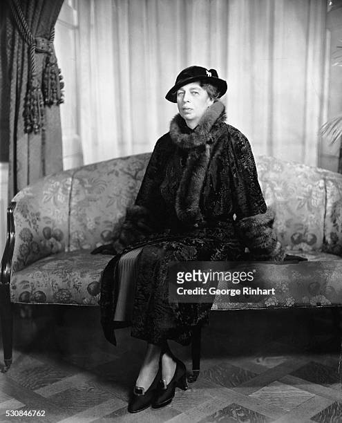 FIRST LADY ELEANOR ROOSEVELT IN A FUR-COLLARED COAT WITH FUR CUFFS. SHE IS SITTING ON A FLOWERED SOFA. UNDATED PHOTOGRAPH.