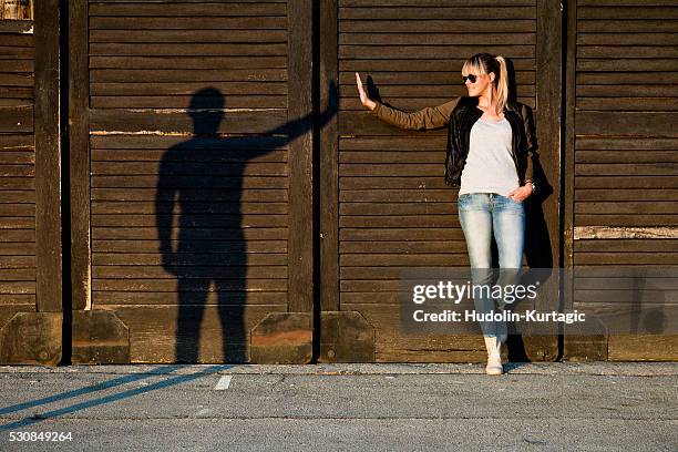 young woman gesturing with silhouette of young man against wooden wall - sillouette cool attitude stock pictures, royalty-free photos & images