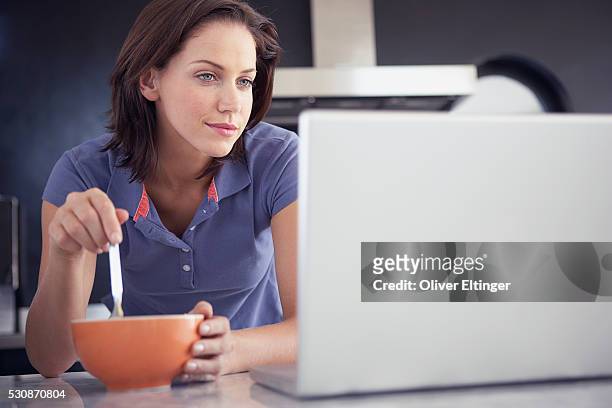 woman eating breakfast and using laptop - oliver eltinger stock-fotos und bilder