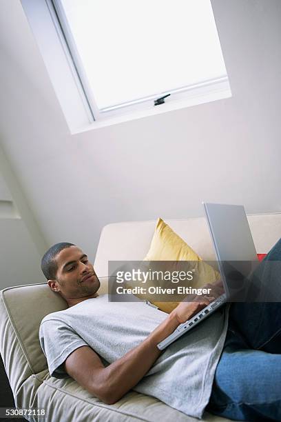 man using laptop computer on couch - oliver eltinger stock-fotos und bilder