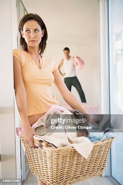 woman with laundry basket, husband with more laundry in background - lazy husband stock pictures, royalty-free photos & images