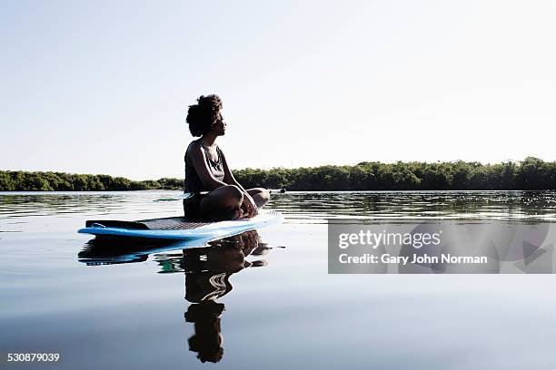 young woman sitting legs crossed on paddle board. - paddleboard stockfoto's en -beelden