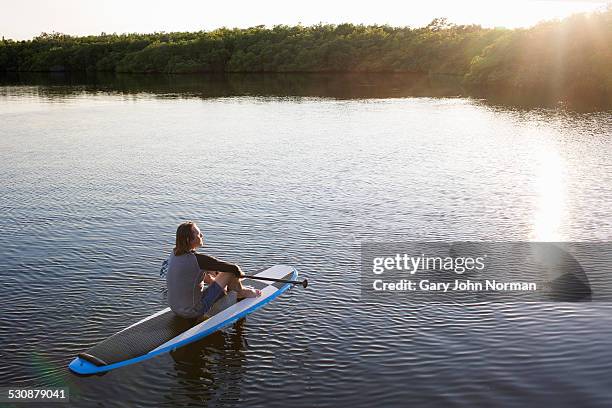 mature man sitting on paddle board on lake. - paddle board men imagens e fotografias de stock