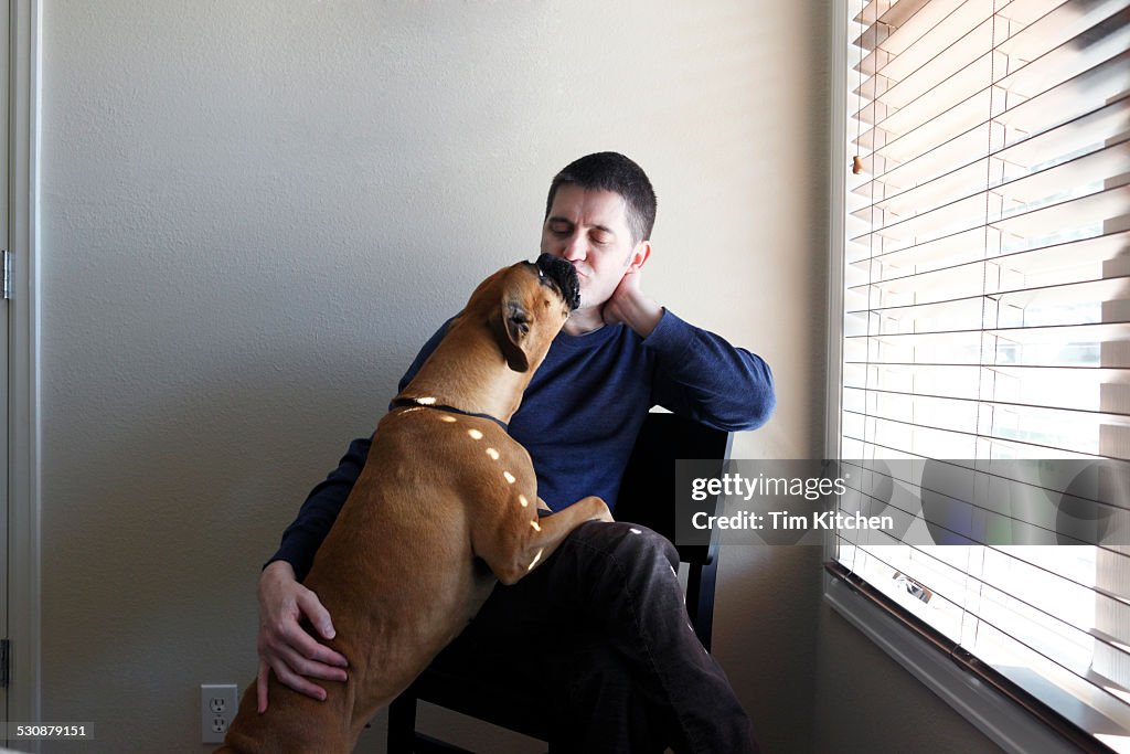 Man sitting in chair being kissed by dog