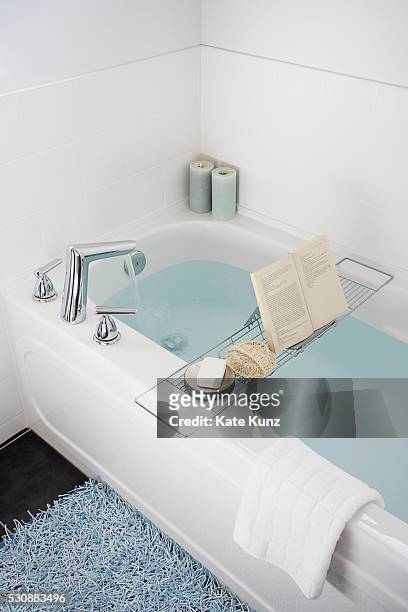 rack over bathtub holding book, soap, and loofah - bath mat stockfoto's en -beelden