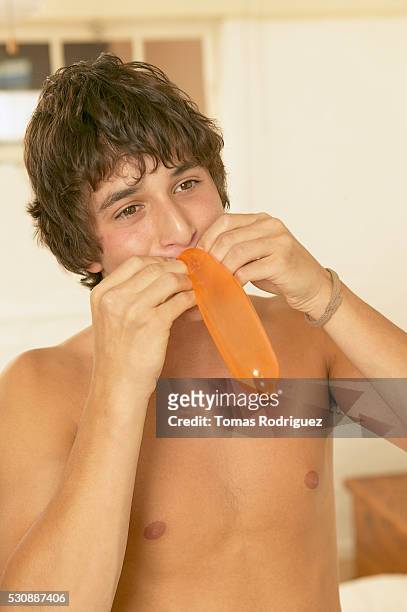 teen boy blowing into orange condom - headshot of a teen boy stockfoto's en -beelden