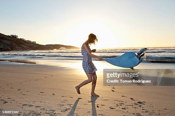 young woman shaking out her towel - telo da mare foto e immagini stock