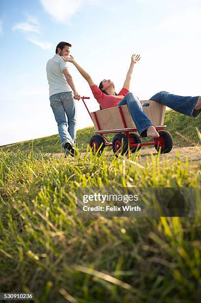 man pulling his girlfriend in a wagon - bollerwagen mann stock-fotos und bilder