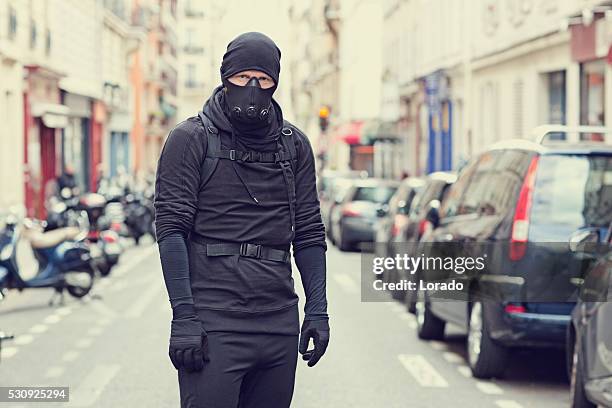 male standing in black in paris street wearing breathing apparatus - street villains stock pictures, royalty-free photos & images