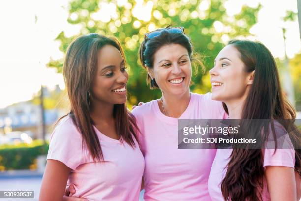 group of diverse women in pink breast cancer awareness shirts - mixed race woman stockfoto's en -beelden