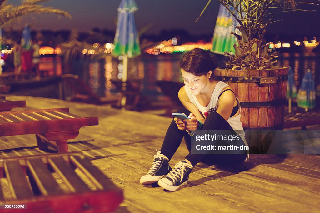 Girl at the beach by night using smartphone