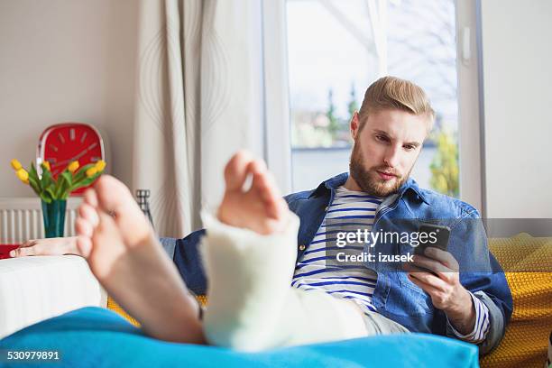 young man with broken leg using smart phone at home - man crutches stock pictures, royalty-free photos & images