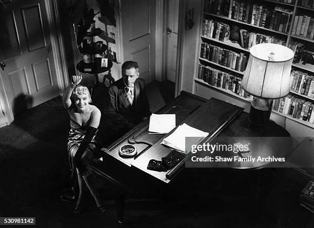 Marilyn Monroe wearing a tiger-striped dress seated at a piano with co-star Tom Ewell waves to the camera in 1954 during the filming of "The Seven...