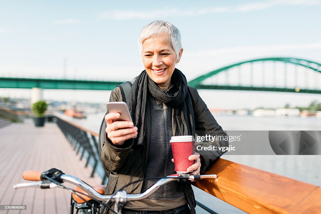 Reife Frau SMS auf Ihr Smartphone und Trinken Kaffee