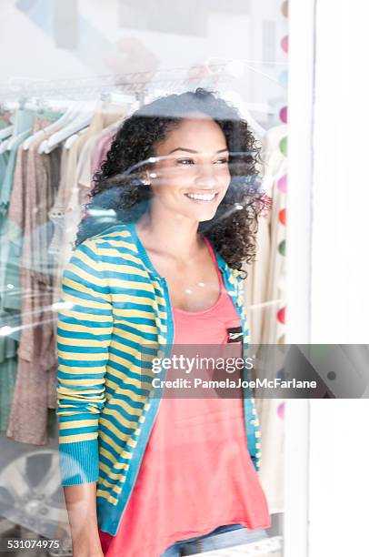 happy african american woman looking out of clothing boutique window - vouyer stock pictures, royalty-free photos & images