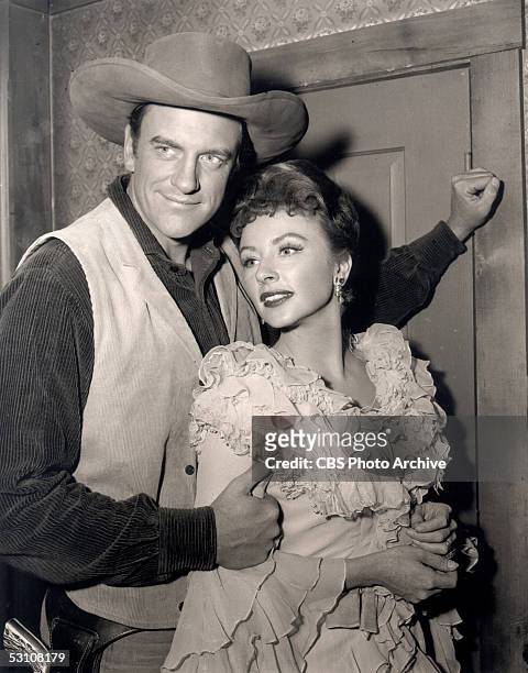 Promotional still of American actors James Arness and Amanda Blake as they embrace and pose in costume from the CBS television western 'Gunsmoke,'...