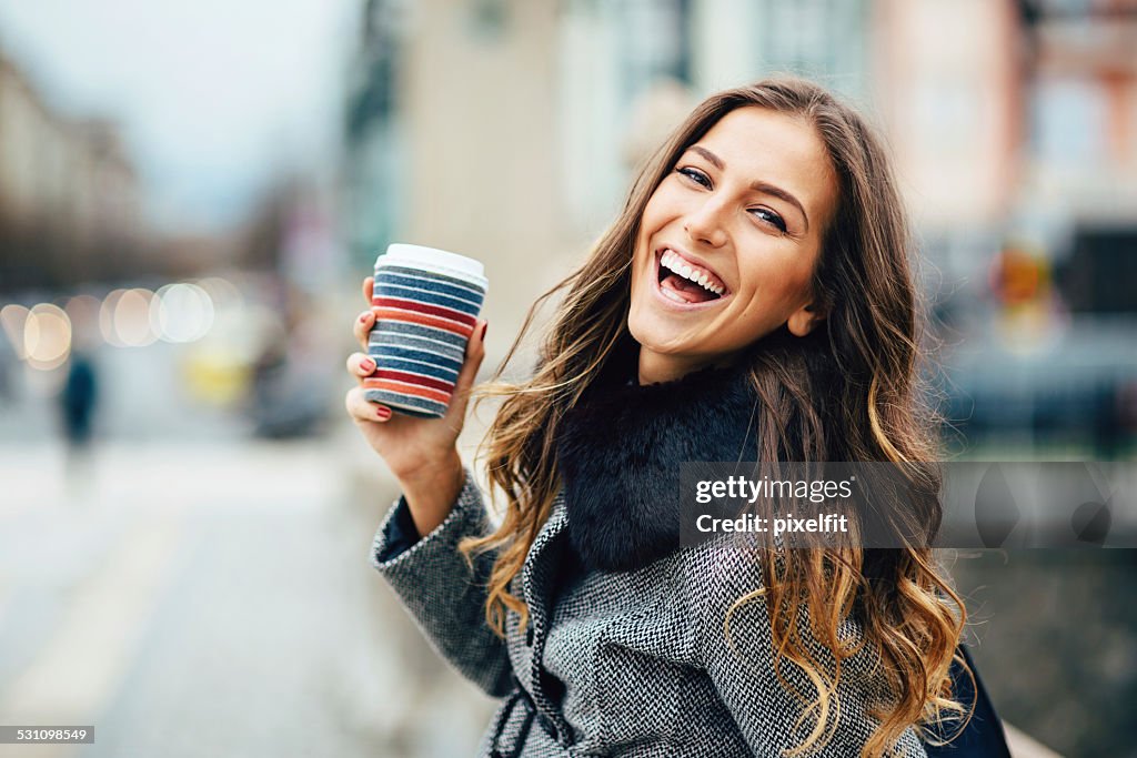 Mujer joven con una taza de café sonriendo al aire libre
