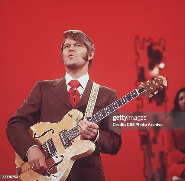 American singer, guitarist, and television host Glen Campbell adjusts a dial on his Ovation Deluxe acoustic - electric guitar in a still from his CBS...