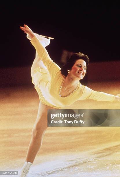 Dorothy Hamill skates on left skate with a big smile bending over at the waist with both arms spread out as her right legs is extended back during...