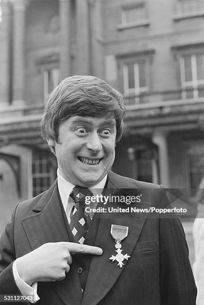 English impressionist Mike Yarwood pictured pointing to his OBE at an investiture ceremony at Buckingham Palace in London on 8th December 1976.