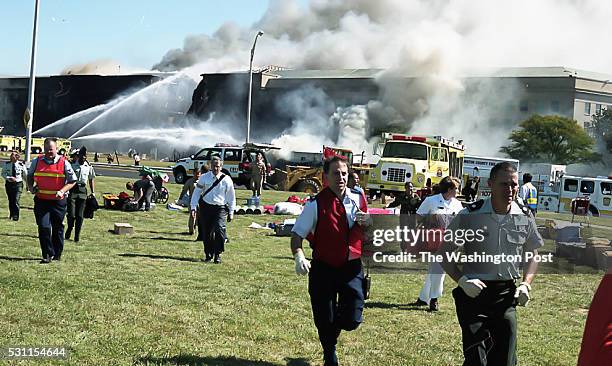 Workers in the foreground attend to people, while firetrucks control flames at the Pentagon building behind, in Arlington, VA on September 11, 2011.