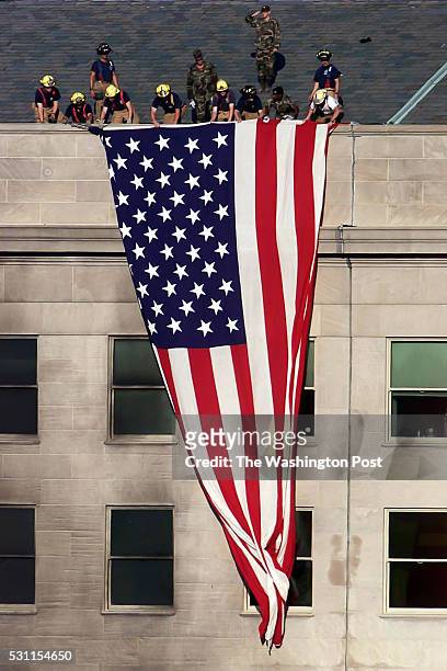 Fire Fighters along with a few military personal drape a large flag over the west wall of the Pentagon a few yards from the area damaged by the...