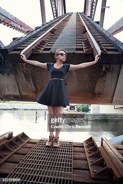 a young woman in a black dress stands in front of a railroad bridge. - bridge gap stockfoto's en -beelden