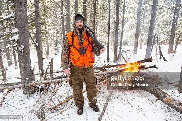 a male hunter stands next to a fire. - spy hunter stock pictures, royalty-free photos & images