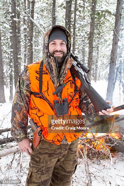a male hunter stands next to a fire. - spy hunter stock pictures, royalty-free photos & images