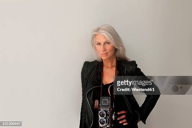 portrait of mature woman with a vintage camera leaning at a wall - arrogancia fotografías e imágenes de stock