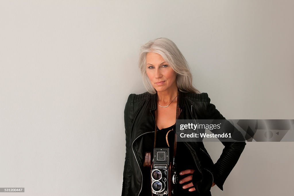 Portrait of mature woman with a vintage camera leaning at a wall