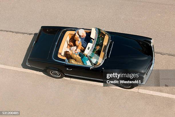 senior couple in convertible car driving down street, elevated view - porsche driving stock pictures, royalty-free photos & images