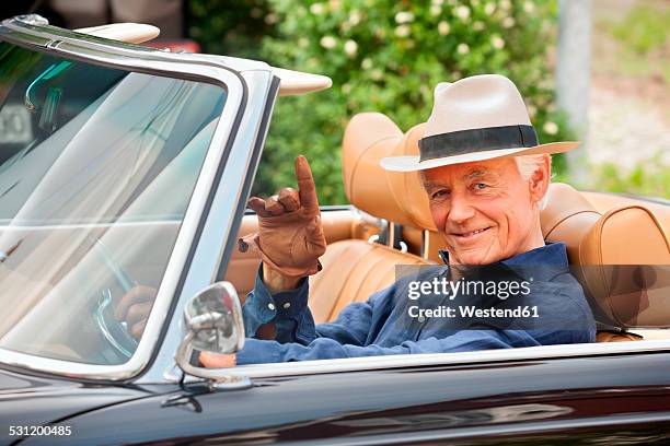 portrait of a smiling senior sitting in a convertible car waving - old car stock-fotos und bilder