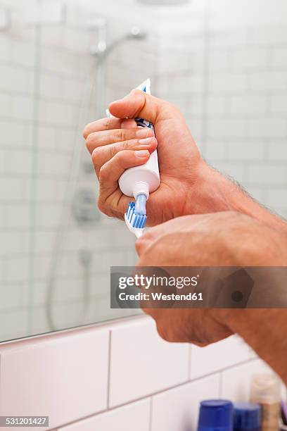 man's hands applying toothpaste on a toothbrush - zahnpasta stock-fotos und bilder