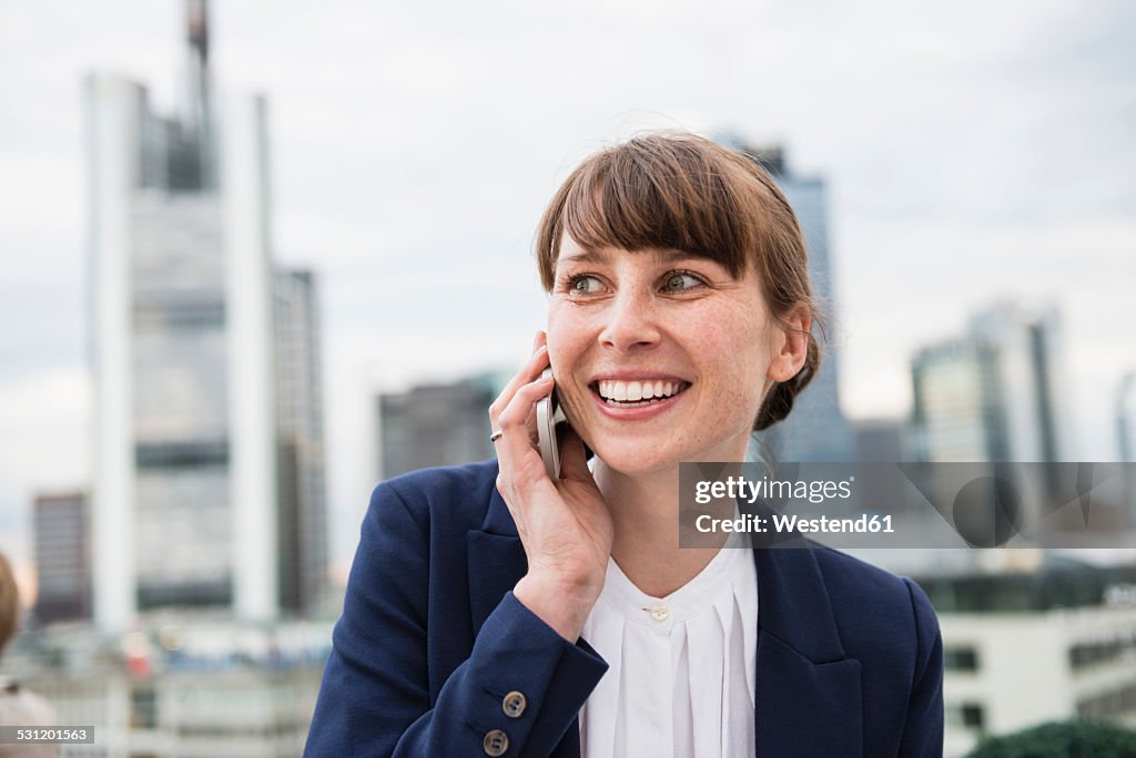 Germany, Hesse, Frankfurt, portrait of smiling businesswoman telephoning in front of skyline