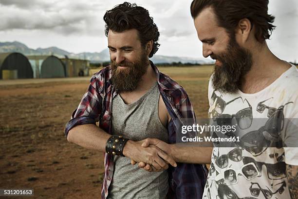 two men with full beards in abandoned landscape shaking hands - masculinidade imagens e fotografias de stock