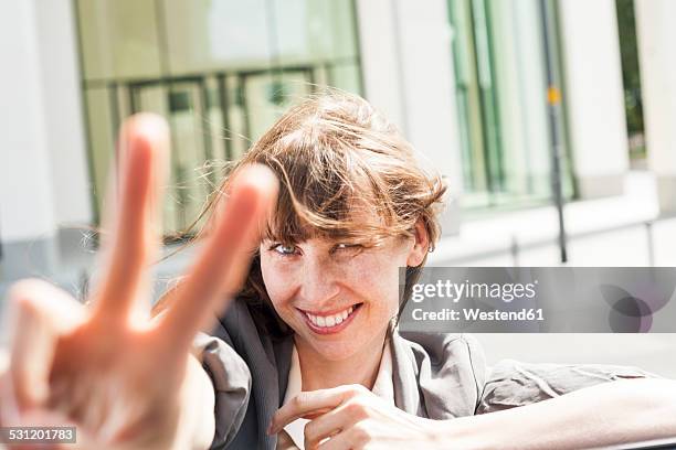 germany, hesse, frankfurt, portrait of smiling businesswoman leaning on car roof showing victory-sign - peace sign gesture stock-fotos und bilder