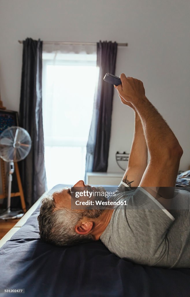 Serious looking man lying on his bed taking a selfie with his smartphone