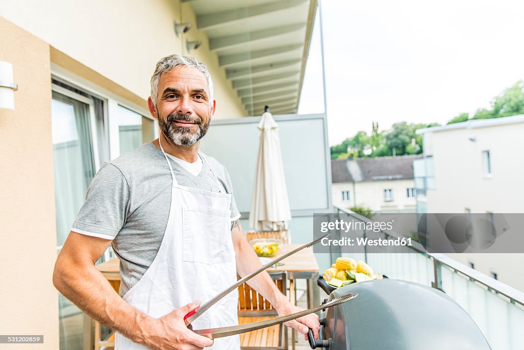 Portrait of smiling man with apron and tongs on his balcony